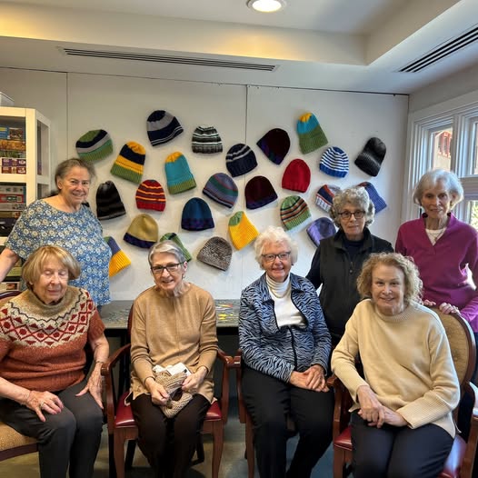 older women pose in front of knit caps they created.