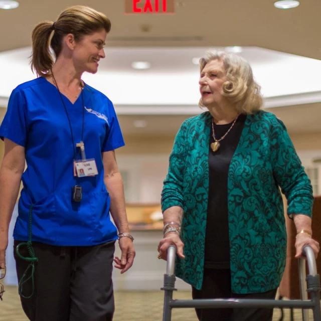 Nurse and senior woman walking through skilled nursing facility