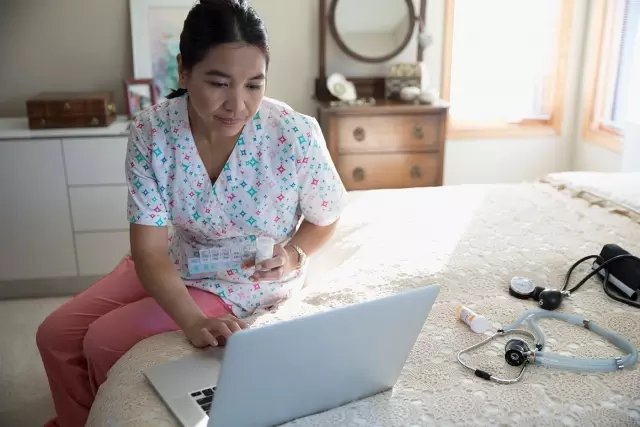 Nurse using laptop on bed