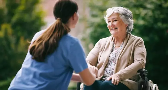 Caregiver and senior resident in wheelchair outdoors