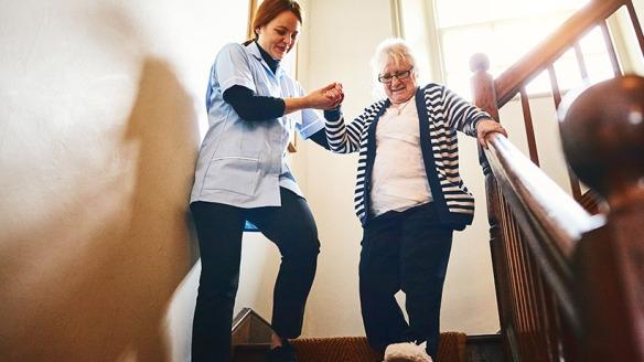 Caregiver helping senior woman walk down stairs