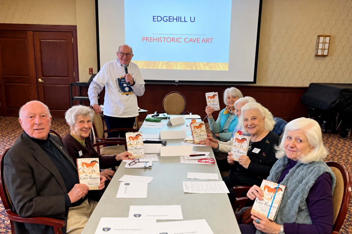 Edgehill residents gather around a table holding books during an Edgehill University program on prehistoric cave art, led by a resident presenter.